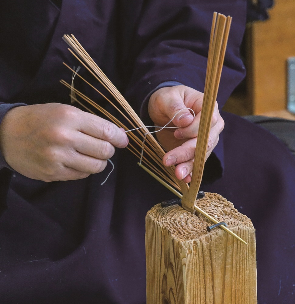 鎌を通し、糸を縛って穂を編む「編み」の工程